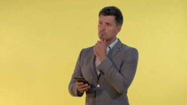 Takım elbiseli uzun bir adam bir eli çenesinde, akıllı telefona bakıyor ve bir şeyler düşünüyor..