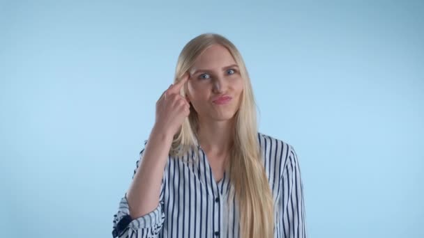 Приваблива жінка скручує індексний палець у храмі на синьому фоні . — стокове відео