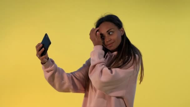 Cheerful mixed-race lady making selfie on smartphone on yellow background. — Stock Video