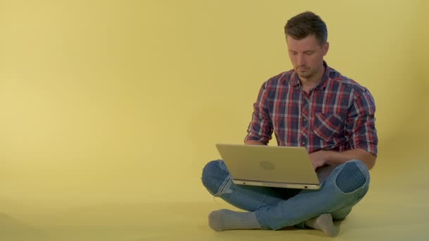 Привлекательный молодой человек болтает с друзьями за компьютером, сидя на полу — стоковое видео