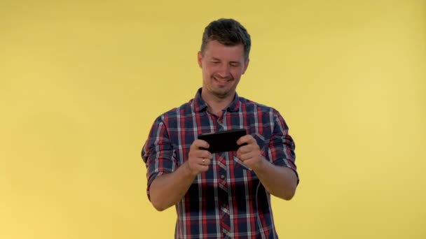 Позитивный молодой человек любит играть в онлайн игры на смартфоне на желтом фоне — стоковое видео