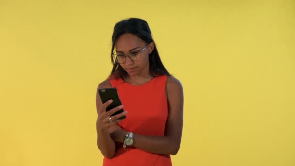 Mujer bonita Multiracial mirando sorprendido en el teléfono inteligente sobre fondo amarillo . — Vídeos de Stock