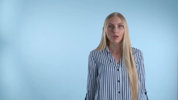 Blondýny mladá žena roztahuje ruce do stran a říká "co" na modrém pozadí. — Stock video