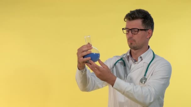 Крупный план молодого врача в халате и очках, смотрящего на фляжку с голубой жидкостью — стоковое видео