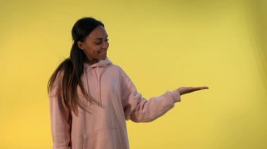 Güzel Afrikalı kadın boş elle sarı arka planda bir şey sunuyor..