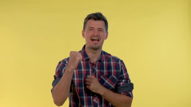 Izgatott fiatalember kiabál és ökölbe szorítja a kezét a sárga háttér. — Stock videók
