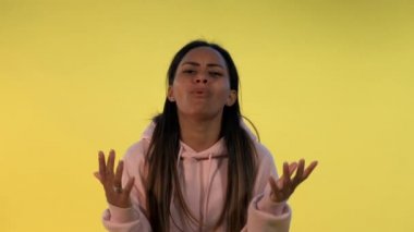 Çaresiz çoklu etnik kökenli kadın sarı arka planda ellerini yana açıyor..