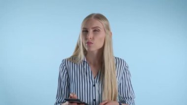 Sarışın genç bir kadın mavi arka planda bir şey düşünürken çenesini eliyle tutuyor..
