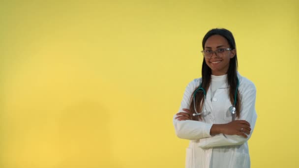 Nero medico femminile in camice da laboratorio sorridente alla fotocamera su sfondo giallo . — Video Stock