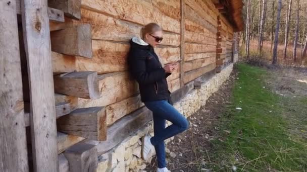 Egy nő okos telefont használ egy faház mellett egy régi faluban.. — Stock videók