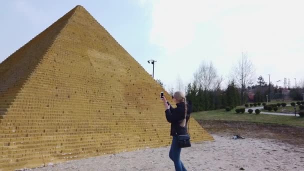 Flicka tar ett foto nära en liten egyptisk pyramid. Miniatyrpark. — Stockvideo