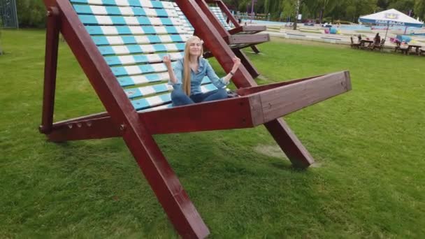Flickan mediterar på en mycket stor solstol i parken. — Stockvideo