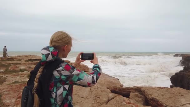 Chica se para con su espalda y toma una foto en su teléfono celular el mar. Movimiento lento — Vídeos de Stock