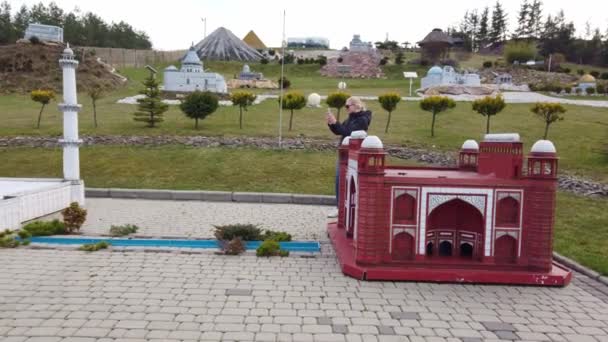 Mulher faz foto andando a pé perto de um modelo em miniatura do edifício Taj Mahal. Parque de Miniaturas . — Vídeo de Stock