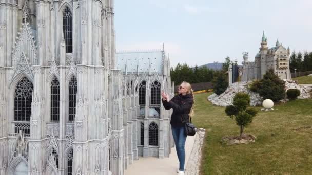 Donna fa foto camminare a piedi vicino a un modello in miniatura della vecchia Cattedrale, Europa. Parco delle Miniature. — Video Stock