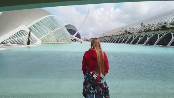 Молода жінка дивиться на нове сучасне місто в сонячний день і піднімає руки вгору. — стокове відео