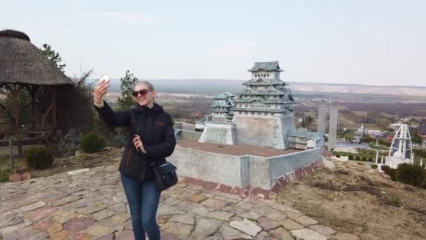 Fille prend un selfie près d'une pagode japonaise chinoise miniature. Parc des Miniatures. — Video