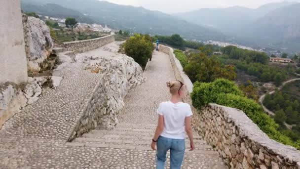 Szőke nő sétál védekező falak középkori vár Európában hegyek. — Stock videók