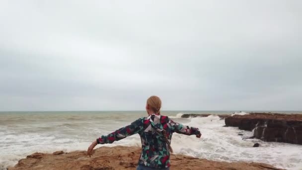 Ragazza alza le mani mentre in piedi con la schiena sulla riva del mare durante una tempesta. — Video Stock