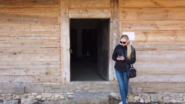 Frau benutzt Handy in der Nähe eines Holzhauses in einem alten Dorf. — Stockvideo