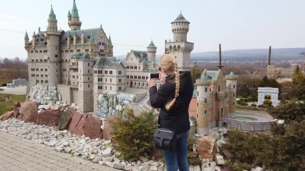 Kvinna gör foto promenader till fots nära en miniatyr modell av det gamla slottet Neuschwanstein, Tyskland. Miniatyrpark. — Stockvideo