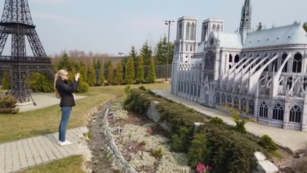 Kvinna gör foto promenader till fots nära en miniatyr modell av den gamla Notre Dame Cathedral, Frankrike. Miniatyrpark. — Stockvideo