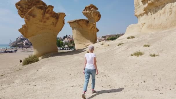 Девушка, идущая по пустыне рядом с желтой футуристической скалой. — стоковое видео