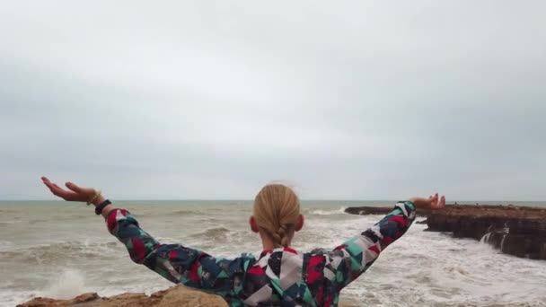 Girl raises her hands up while standing with her back on the seashore during a storm. — Stock Video