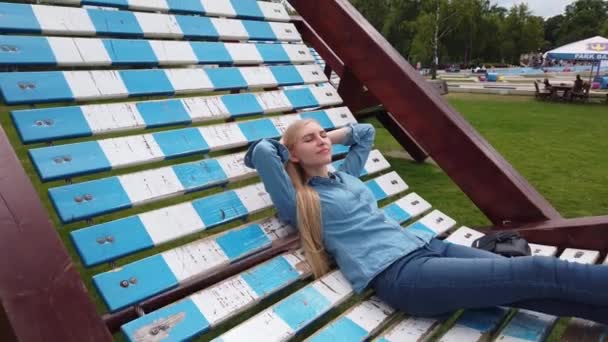 Дівчинка лежить на дуже великому палубному стільці в парку.. — стокове відео