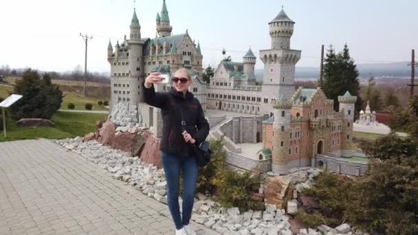Donna prende un selfie vicino a un modello in miniatura del vecchio castello Neuschwanstein, Germania. Parco delle Miniature. — Video Stock
