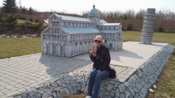 Kvinnan tar en selfie nära en miniatyrmodell av den gamla katedralen, Europa. Miniatyrpark. — Stockvideo