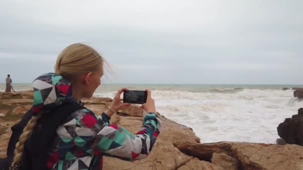 Дівчина стоїть зі спиною і фотографується на своєму мобільному телефоні. Повільний рух — стокове відео