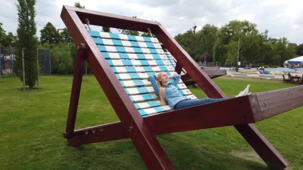 Самки лежать на дуже великому палубному стільці в парку.. — стокове відео