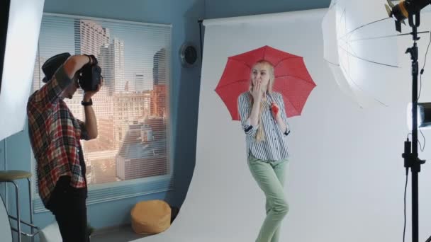 Bakom kulisserna på fotografering: attraktiv kaukasisk modell poserar med rött paraply — Stockvideo