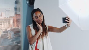 Fotoğraf çekiminde, güzel bir Afrikalı model profesyonel stüdyoda akıllı telefondan selfie çekiyor.