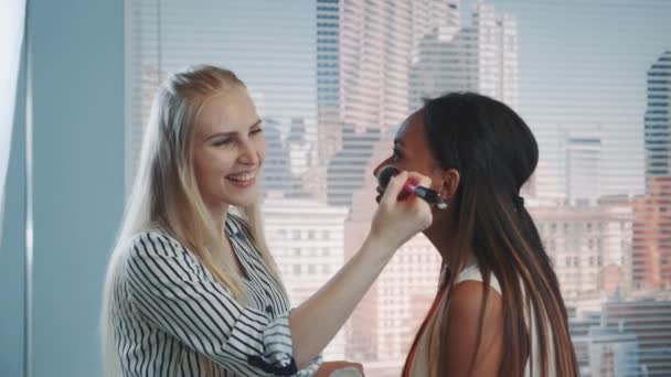 Close-up dari make-up artist menerapkan makeup pada model hitam dengan pencakar langit di latar belakang — Stok Video