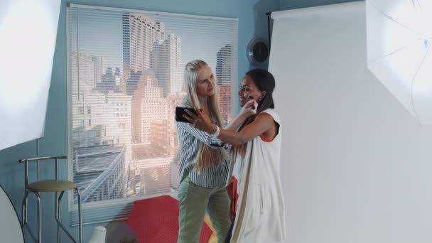 Modelo preto famoso fazendo selfie com artista de maquiagem enquanto ela aplica maquiagem — Vídeo de Stock