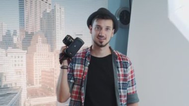 Profesyonel kamerayla gülümseyen ve poz veren sıradan giyinmiş genç fotoğrafçının portresi.