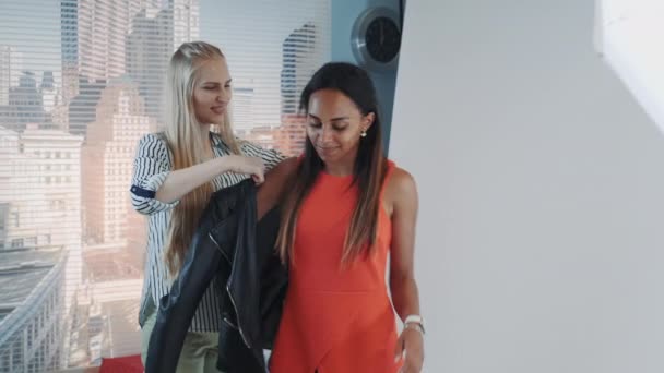 Primer plano del asistente femenino ayudando a la modelo africana a usar chaqueta durante la sesión de fotos en el estudio — Vídeos de Stock