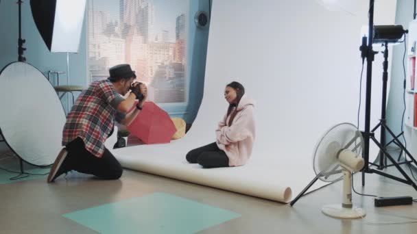 Tras bastidores de la sesión de fotos: modelo negro posando en el suelo para un fotógrafo . — Vídeos de Stock