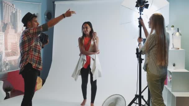 Za kulisami sesji zdjęciowej: fotograf proszący asystenta o skierowanie oświetlenia do modelki — Wideo stockowe