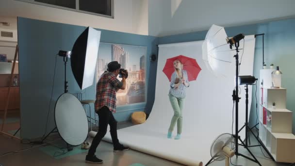 Tras bastidores de la sesión de fotos: hermosa modelo rubia posando con paraguas rojo — Vídeo de stock