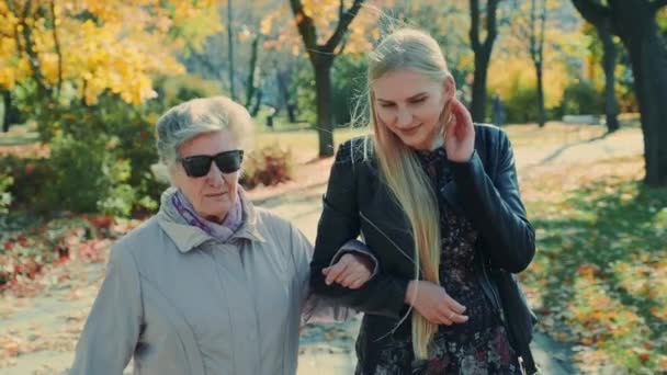 Vieja caminando junto con la alegre chica rubia en el parque de otoño — Vídeos de Stock