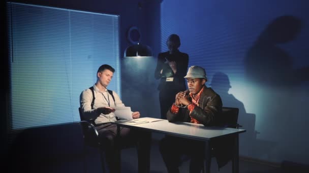 Black prisoner in handcuffs having interview with caucasian detective in interrogation room — Stock Video