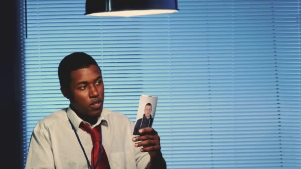Zbliżenie młodego detektywa mieszanej rasy pokazujące zdjęcia podejrzanej osoby — Wideo stockowe