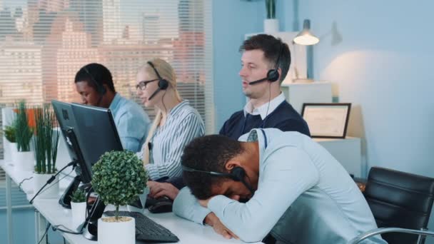 Mixed-race customer support operator falling asleep on his table in call center — Stockvideo