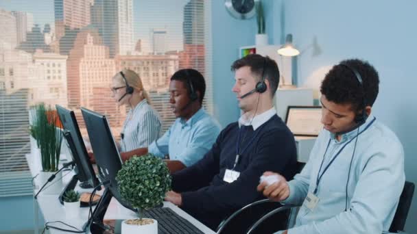 Multiracial call center agent, bored at work, throwing crumpled paper at his colleague — Stok video