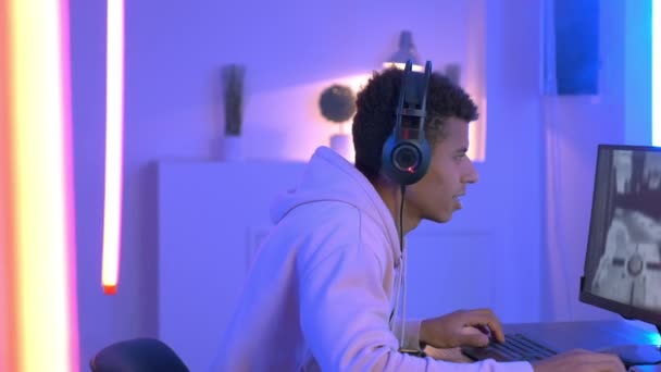 Medium shot of young black gammer in headphones playing in online shooter — ストック動画