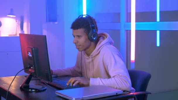 Medium shot of Persistent African gamer παίζοντας online shooter στον υπολογιστή στο δωμάτιο νέον — Αρχείο Βίντεο