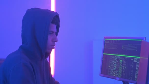 Profile view of african hacker in hoodie working in room filled with display screens — Stock videók